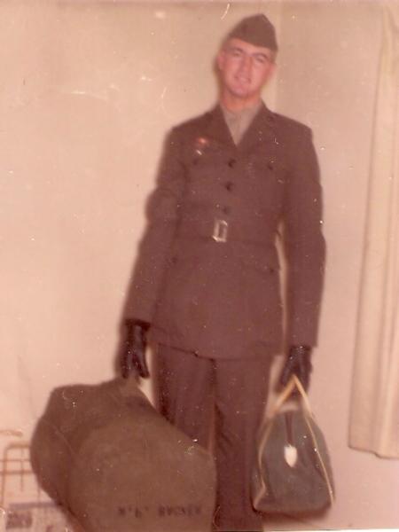 This image shows a service member in a formal military uniform, standing indoors as if preparing to depart or having just arrived.