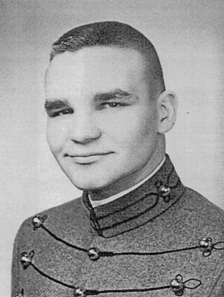 This is a black‑and‑white formal portrait of a young cadet, wearing a highly structured military‑style academy uniform.