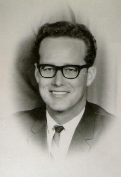 This portrait shows a man in a mid‑20th‑century formal studio photograph, dressed in a suit and tie.