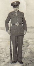 Private First Class Ernest W Kjellerson in uniform standing with rifle photo