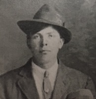 A vintage, black-and-white portrait of Ingvald Gjertson wearing a dark suit jacket, a necktie, and a fedora-style hat.
