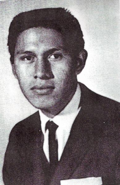 This is a black‑and‑white portrait of Ronald Goodiron dressed formally in a suit and tie. His hair is neatly styled, and he faces the camera directly with a calm, neutral expression.