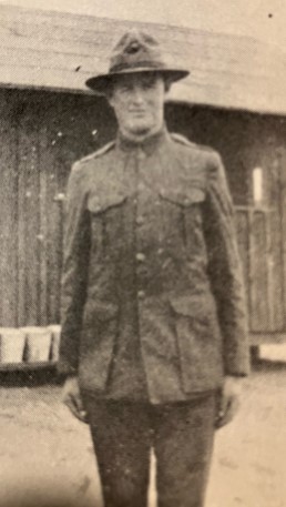 A vintage black-and-white portrait of Private Harley Berton Gallup a World War I-era soldier standing in front of a wooden building.