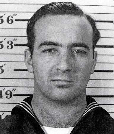 Motor Machinist's Mate First Class Robert B Jenckes in uniform standing in front of height measuring board photo