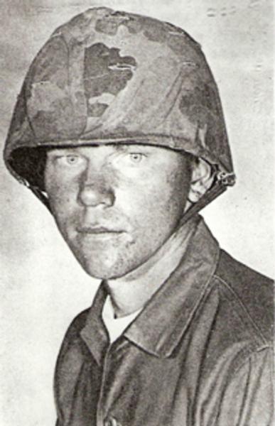 Kenneth Johner black and white photo wearing a combat helmet with a camouflage cover. 