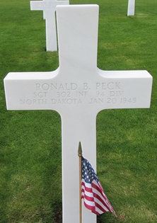 Sergeant Ronald B Peck cross grave marker with small American Flag photo
