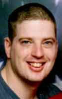 portrait of Jon Paul Fettig with short, dark hair, with the American flag as a backdrop