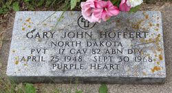 Gary Hoffert photo of a flat, rectangular military gravestone made of light‑colored stone, weathered with age and touched by patches of moss or lichen.