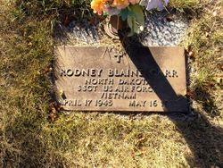 This is a bronze military grave marker honoring Rodney Blaine Orr, set into a concrete frame and surrounded by grass, with a bouquet of artificial flowers placed above it.