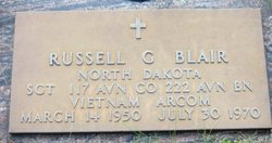 This is a bronze military grave marker honoring Russell G. Blair, set into a concrete frame and surrounded by grass. The design follows the standardized style used for U.S. military memorial plaques.